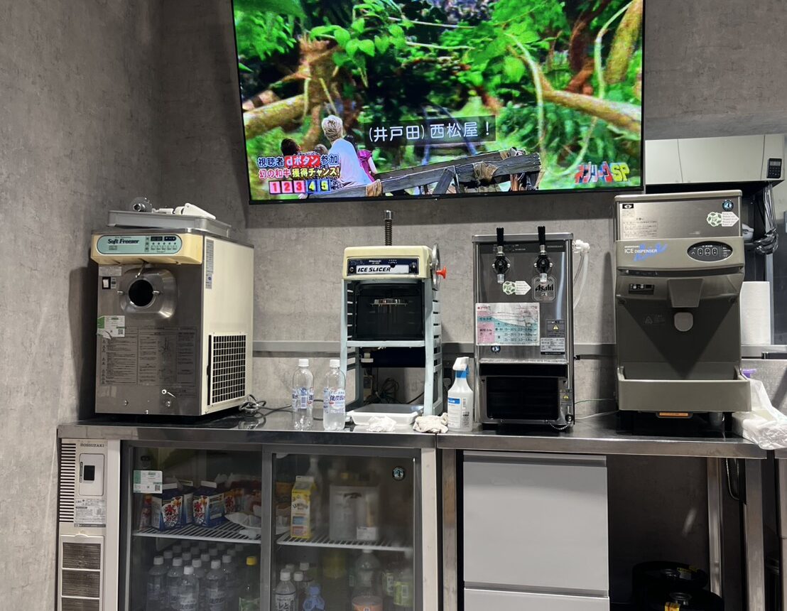 AISAI BASEに設置されたドリンク冷蔵庫と厨房機器、大型モニターの様子