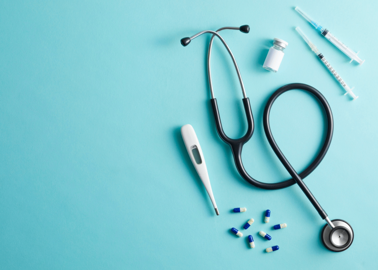 青い背景の上に並べられた体温計や聴診器、注射器、カプセル薬などの医療器具