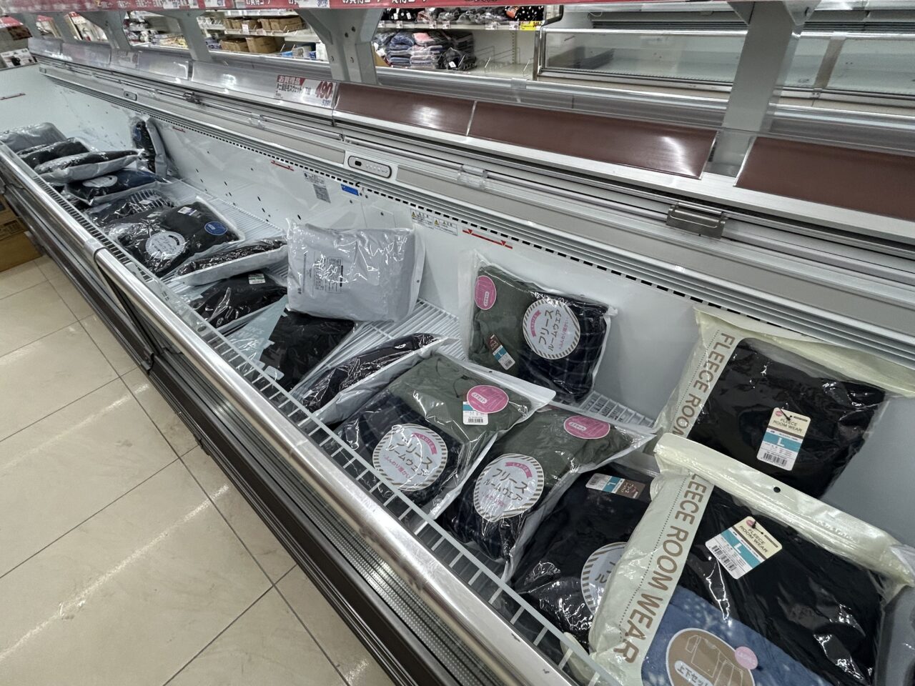 本来は冷凍食品を入れるオープン冷凍庫の中に、パッケージに入ったフリースルームウェアなどの衣類が陳列されている様子