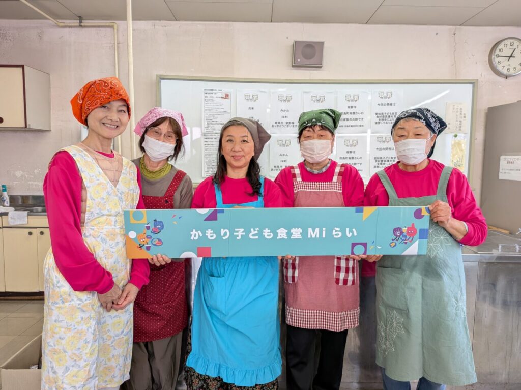 津島市の神守小学校区コミュニティセンター調理室で看板を掲げるかもり子ども食堂Miらいのボランティアスタッフ