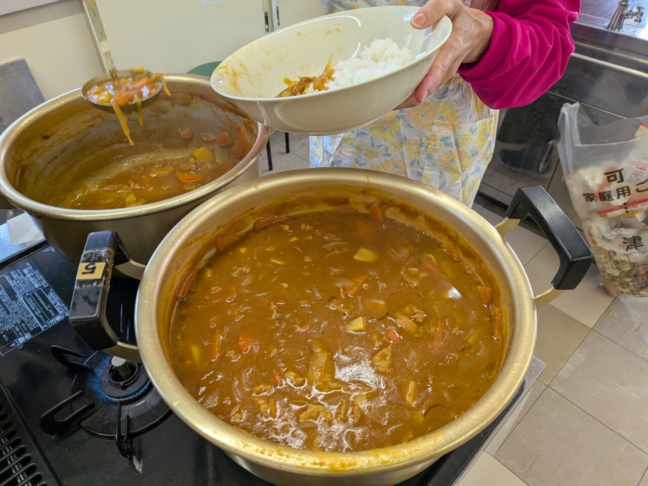 神守小学校区コミュニティセンターの調理室で大きな鍋に入ったカレーを器に盛り付けるボランティアスタッフの様子