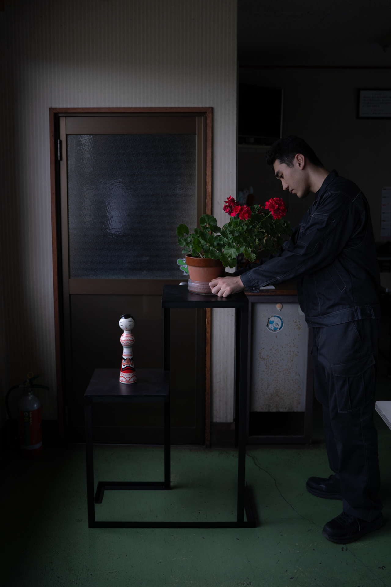 大樹園との盆栽コラボ展示をイメージし工場内で鉄製インテリア什器に赤い花の花瓶を載せて調整する職人